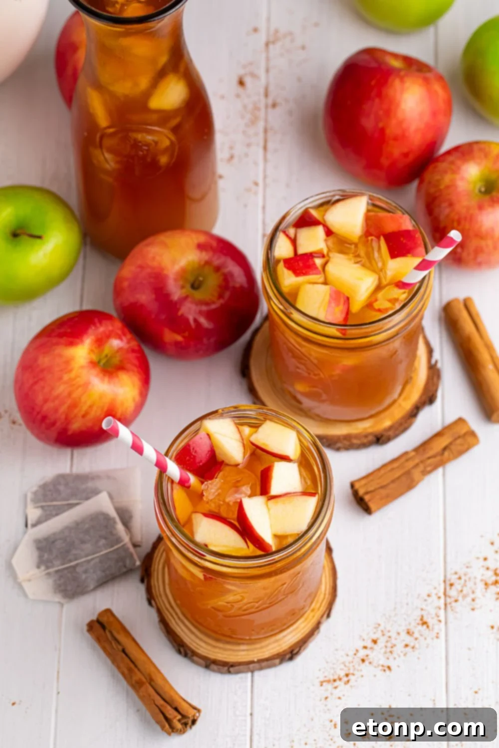 Orchard Apple Iced Tea 13 Apple Cider Iced Teas on table in two glasses, a large pitcher, with tea bags, cinnamon sticks and apples all over table