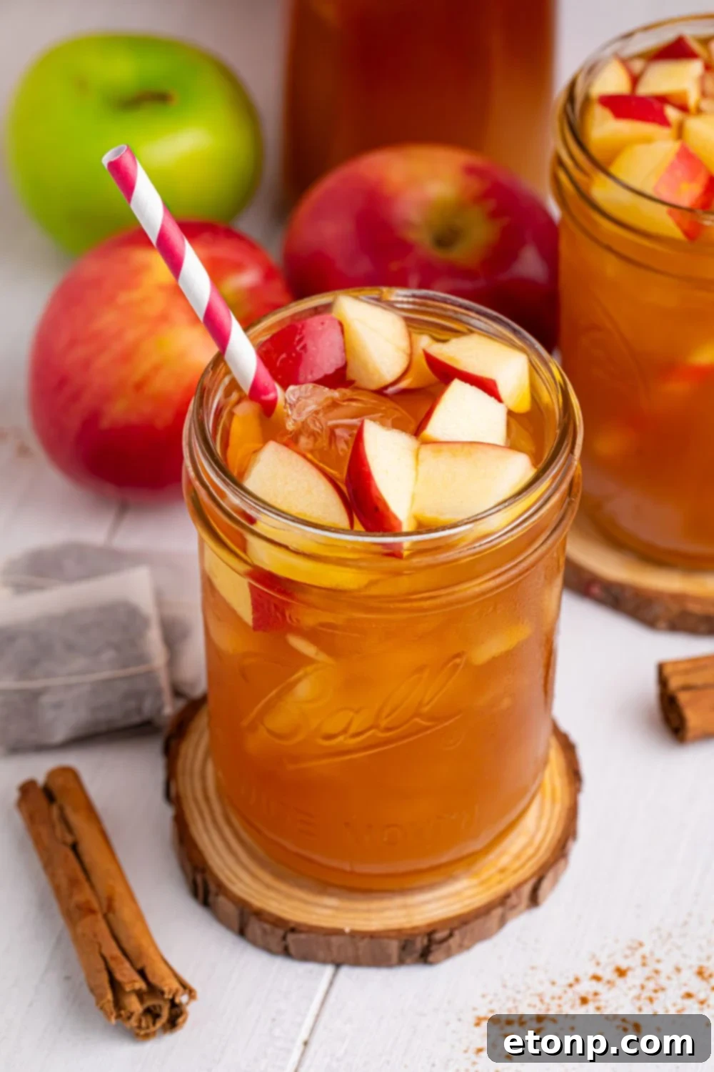 Orchard Apple Iced Tea 17 iced tea ciders in glasses with a cinnamon stick, tea bags, and apples on table around the glasses to show what flavors you will taste in the drink