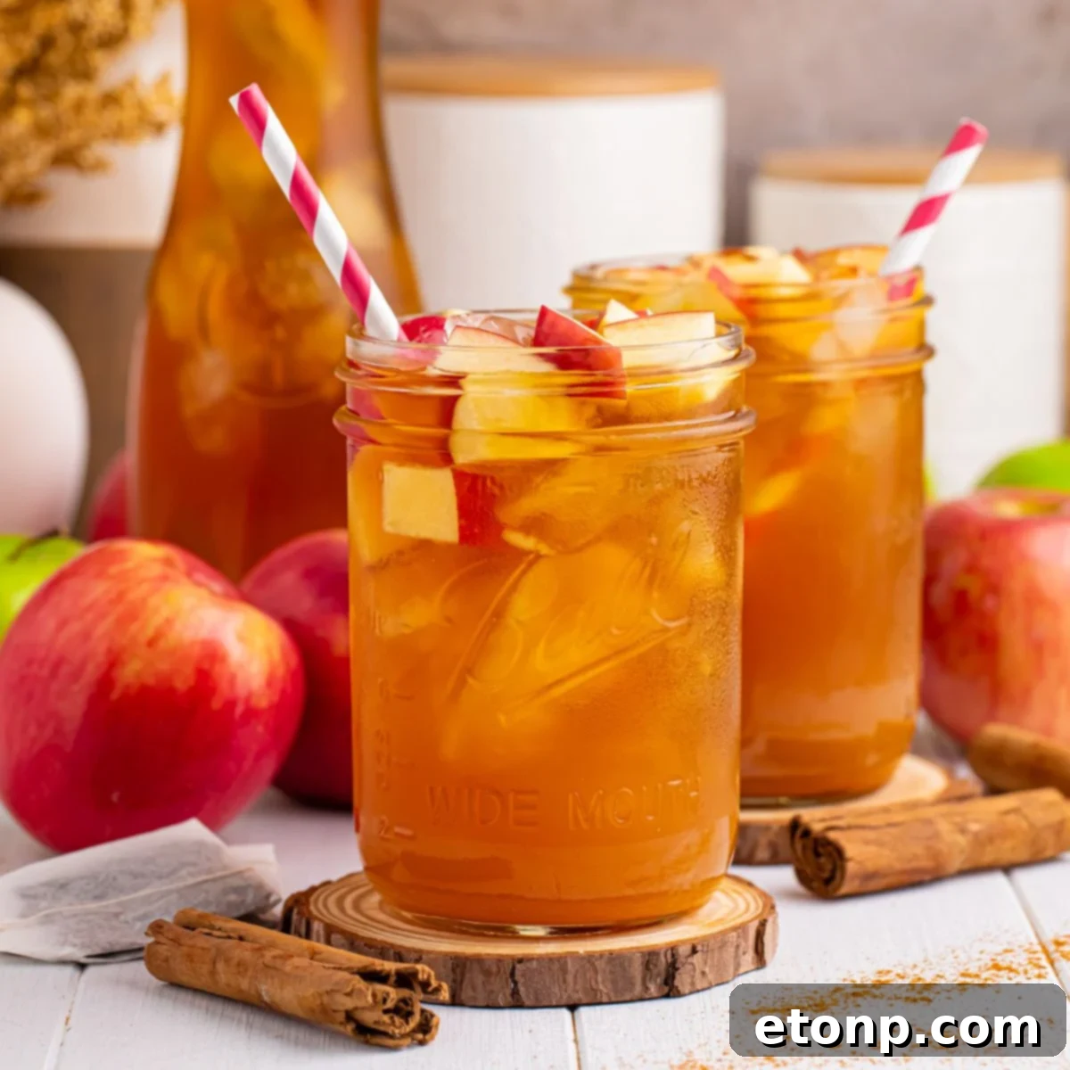 Orchard Apple Iced Tea 3 Apple Cider Iced Tea glasses on table with apples and cinnamon sticks around glasses and a red and white striped straw in each mason glass