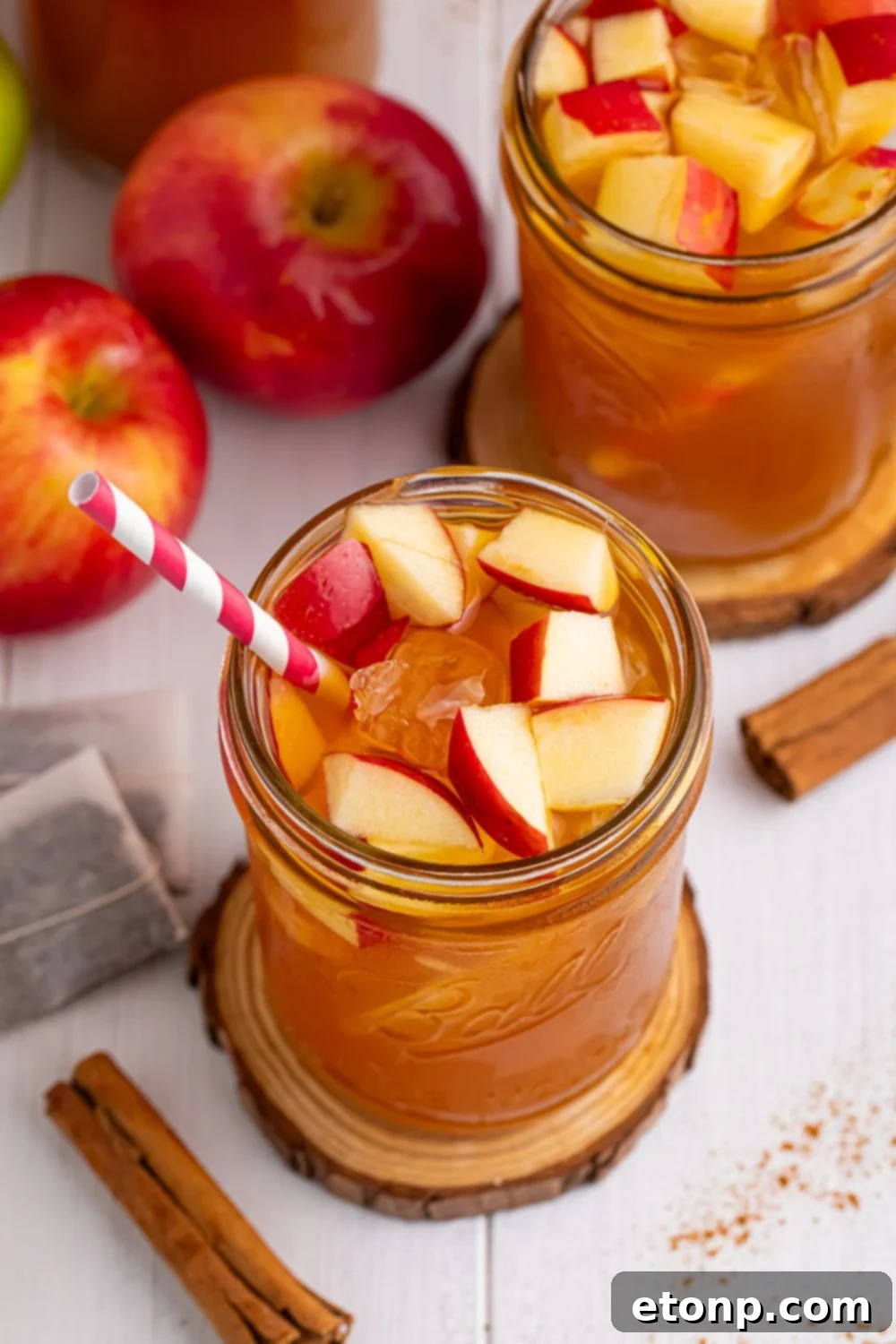 Orchard Apple Iced Tea 4 Apple Cider Iced Teas on table in mason jars with apples and cinnamon sticks spread over the table and fresh diced apples in the glasses