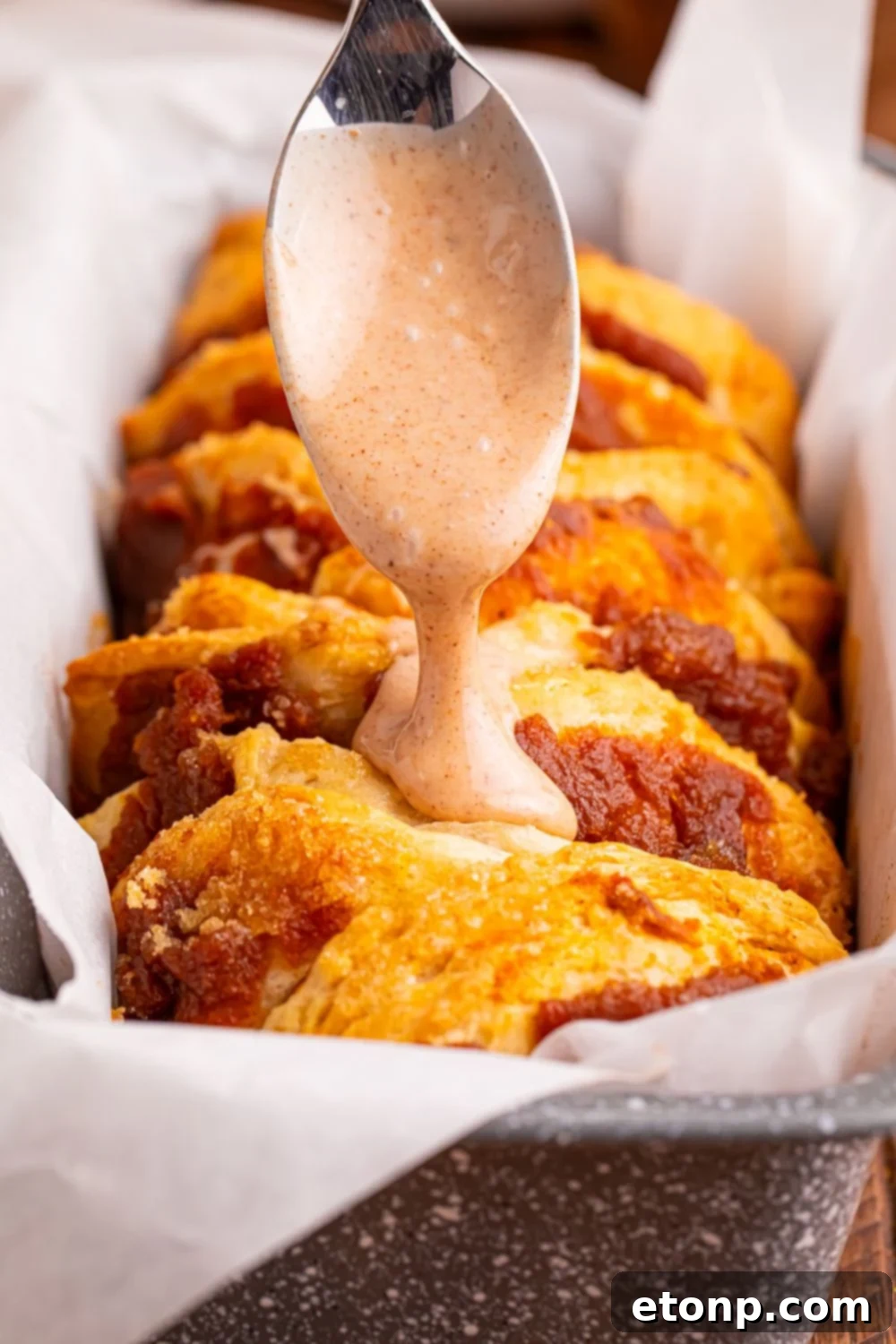 Golden Pumpkin Blossom Bread 3 pumpkin pull apart bread in pan with a maple glaze being drizzled on top with a spoon