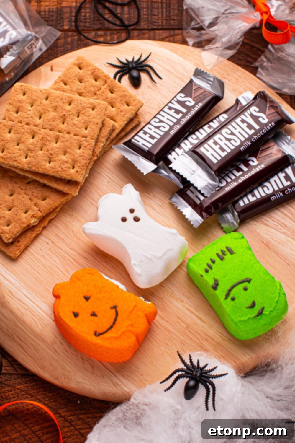 Spooky Smores Treat Packs 6 Halloween Smores Gift Bag ingredients on a round cutting board with plastic spiders and halloween decor around it
