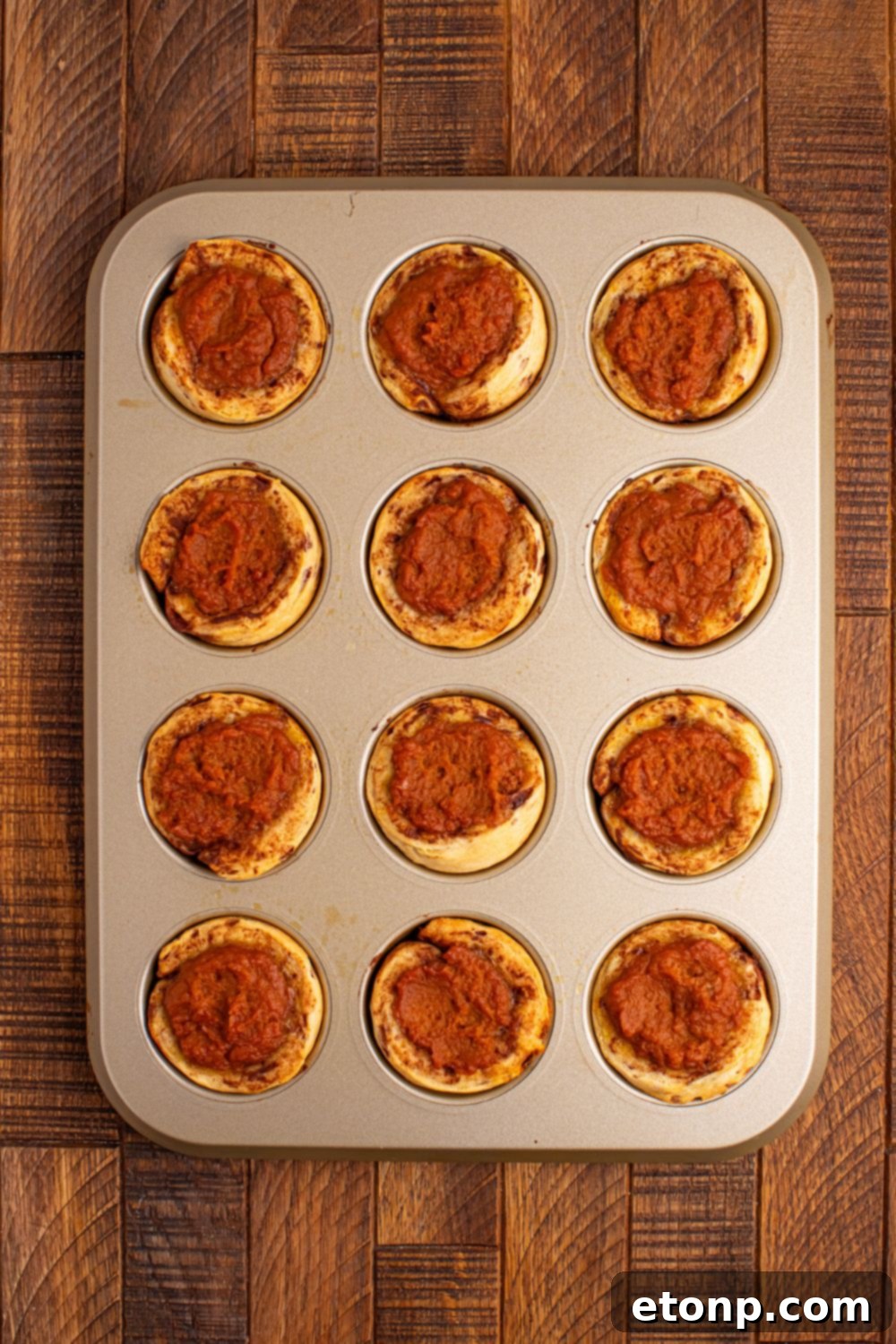 Freshly baked Pumpkin Pie Cinnamon Roll Cups, golden brown and puffed, cooling in a muffin tin after baking.
