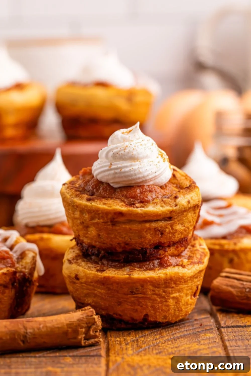 A vibrant display of numerous baked Pumpkin Pie Cinnamon Roll Cups, some stacked, ready for serving.