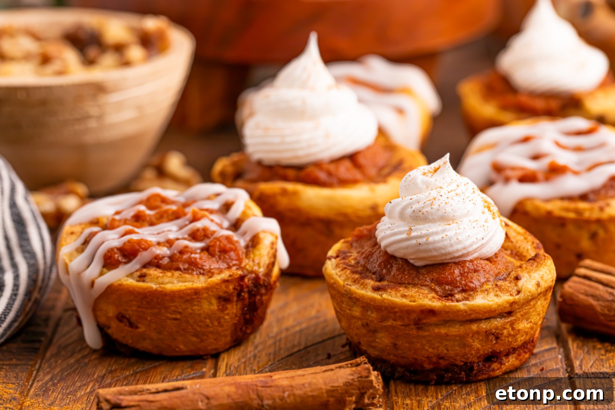 A beautifully baked Pumpkin Pie Cinnamon Roll Cup drizzled with a sweet cinnamon roll glaze, presented on a wooden surface.
