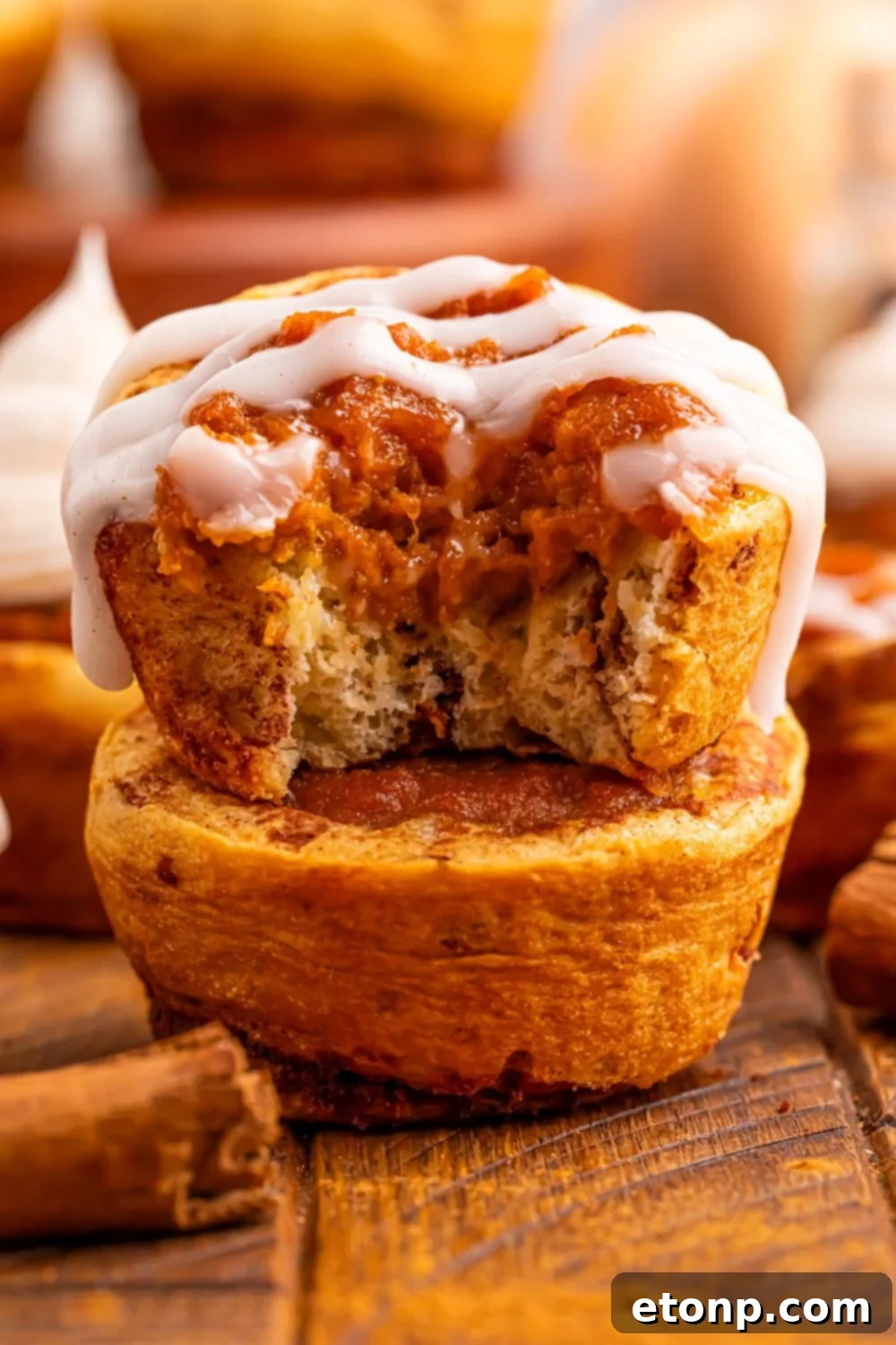 A stack of golden Pumpkin Pie Cinnamon Roll Cups, with one showing a bite taken out, revealing the creamy pumpkin filling within.