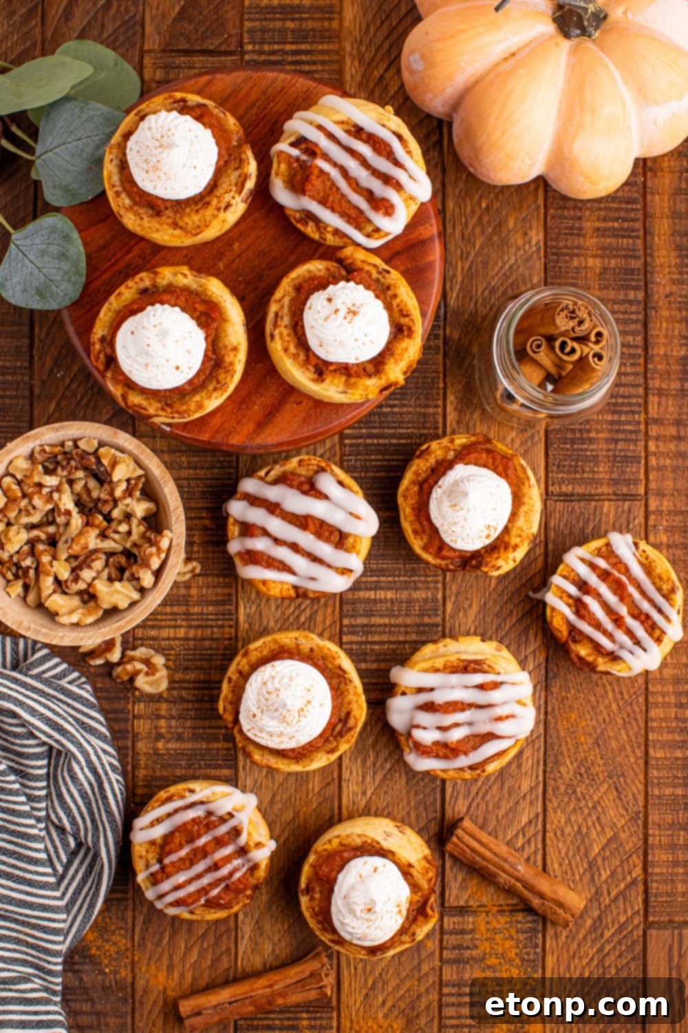A festive overhead view of a table adorned with numerous Pumpkin Pie Cinnamon Roll Cups, surrounded by small bowls of ingredients and a decorative pumpkin.