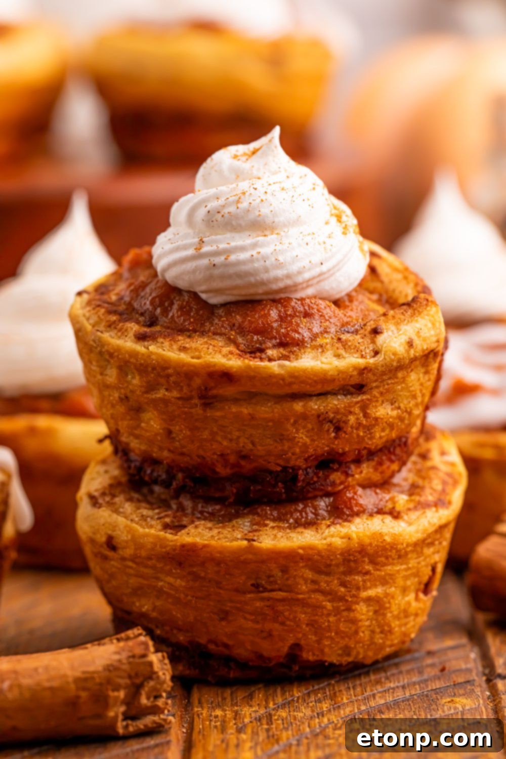 A stack of two Pumpkin Pie Cinnamon Roll Cups on a table, the top one elegantly garnished with a dollop of whipped cream.