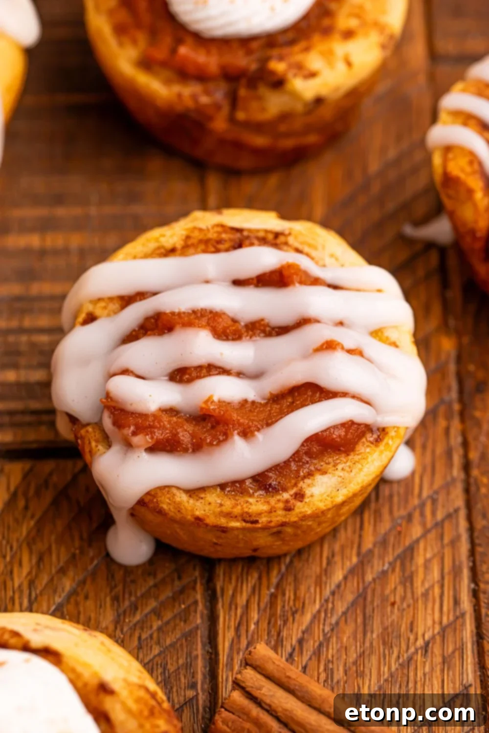 A single Pumpkin Pie Cinnamon Roll Cup on a table, beautifully drizzled with sweet icing.