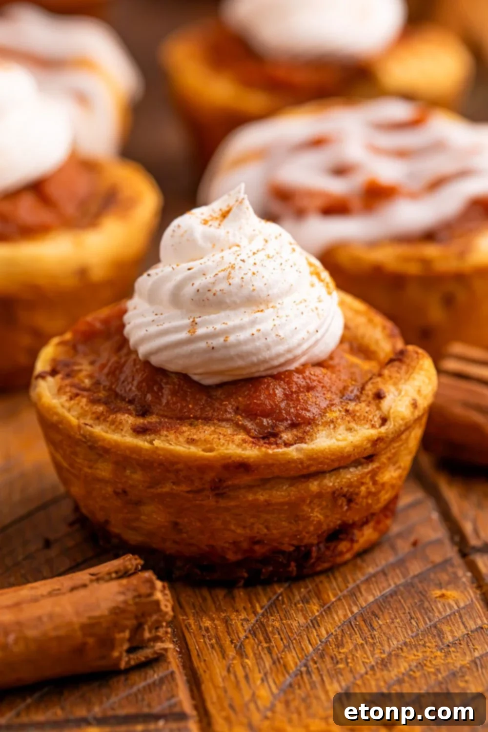 A charming Pumpkin Pie Cinnamon Roll Cup adorned with a generous dollop of whipped cream and a sprinkle of pumpkin spice.