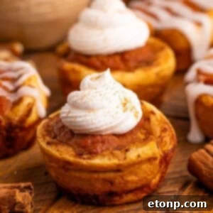 Pumpkin Pie Cinnamon Roll Cups on table with whipped cream on top of some and a icing glaze on others