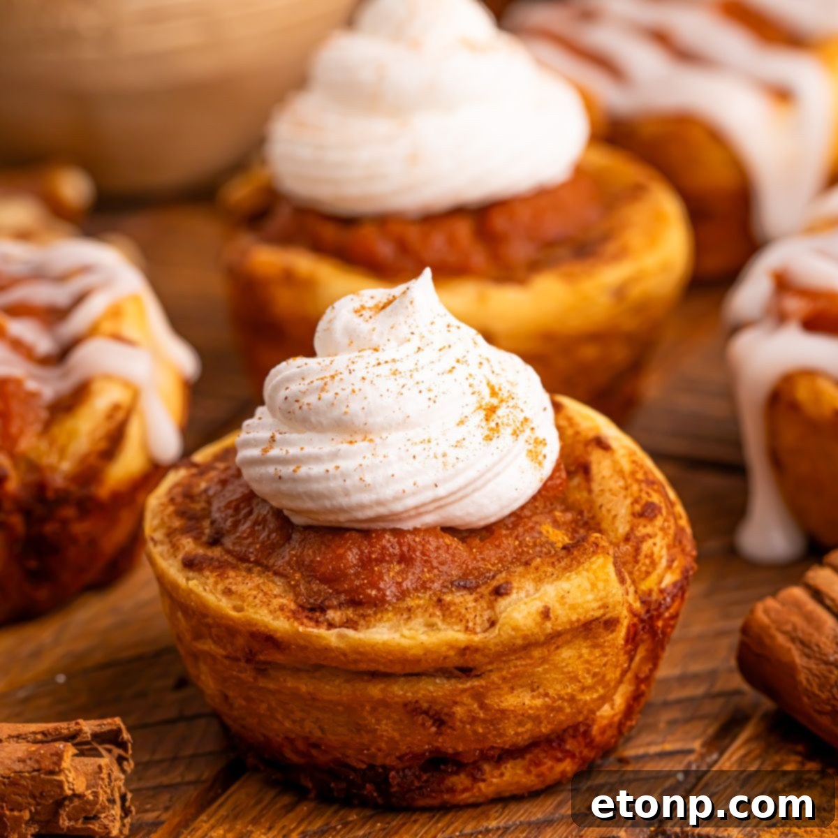 Close-up of freshly baked Pumpkin Pie Cinnamon Roll Cups, some topped with fluffy whipped cream and others with a smooth icing glaze.