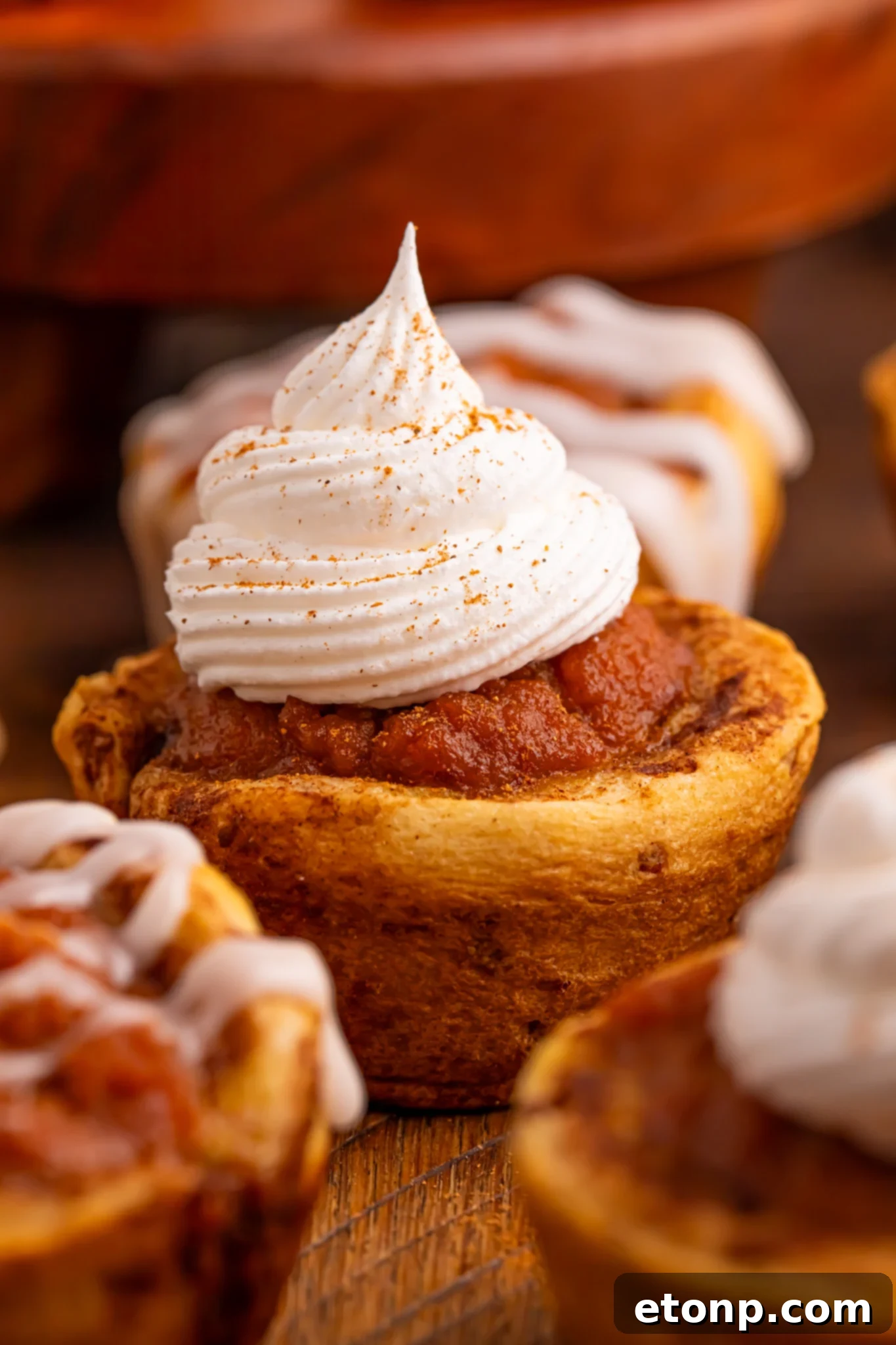An array of golden-brown Pumpkin Pie Cinnamon Roll Cups artfully arranged on a wooden table, showcasing their delightful appearance.