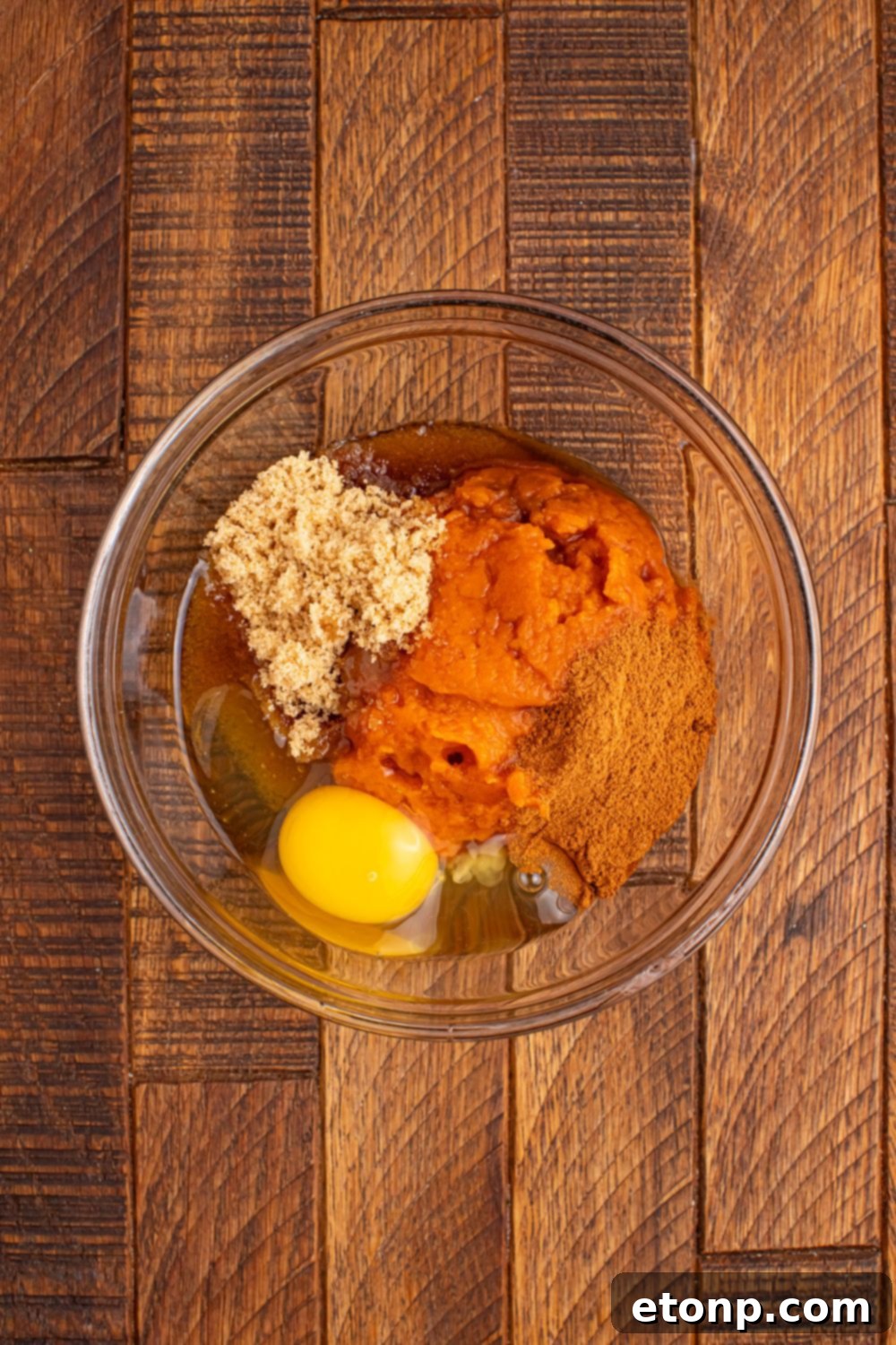 A glass bowl holds the perfectly blended pumpkin pie filling mixture, ready to be added to the cinnamon roll cups.
