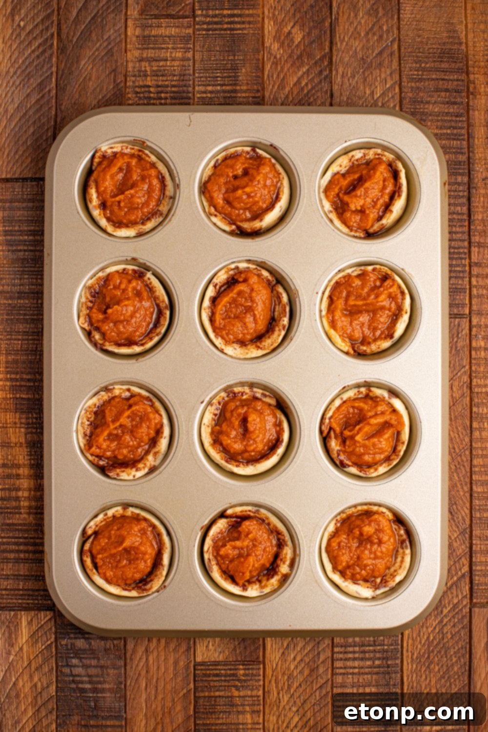 Unbaked Pumpkin Pie Cinnamon Roll Cups, showcasing the raw pumpkin filling nestled within the cinnamon roll dough in a muffin tin.