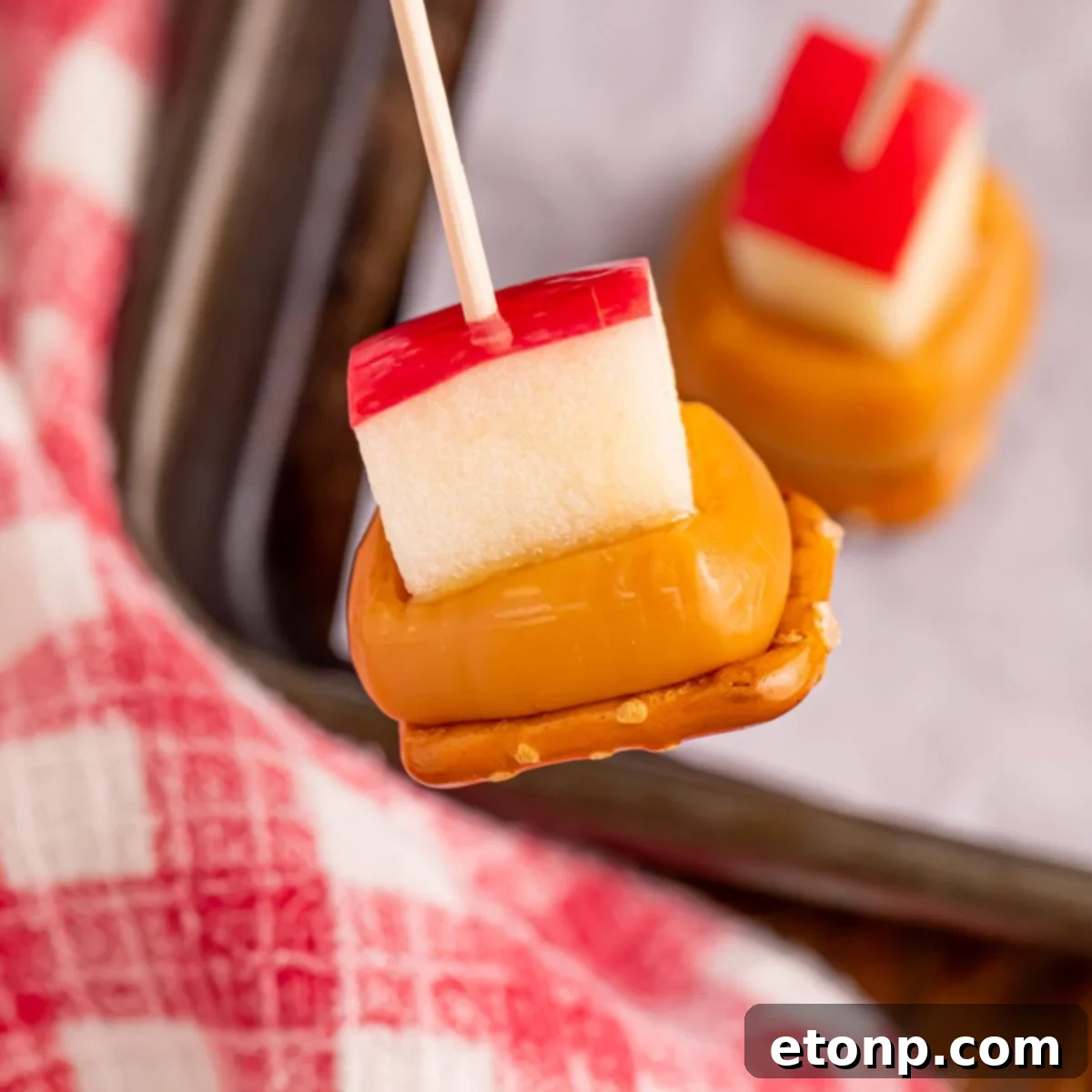 Sweet and Salty Caramel Apple Pretzel Bites 2 Caramel Apple Pretzel Bite on toothpick being held above pan on table