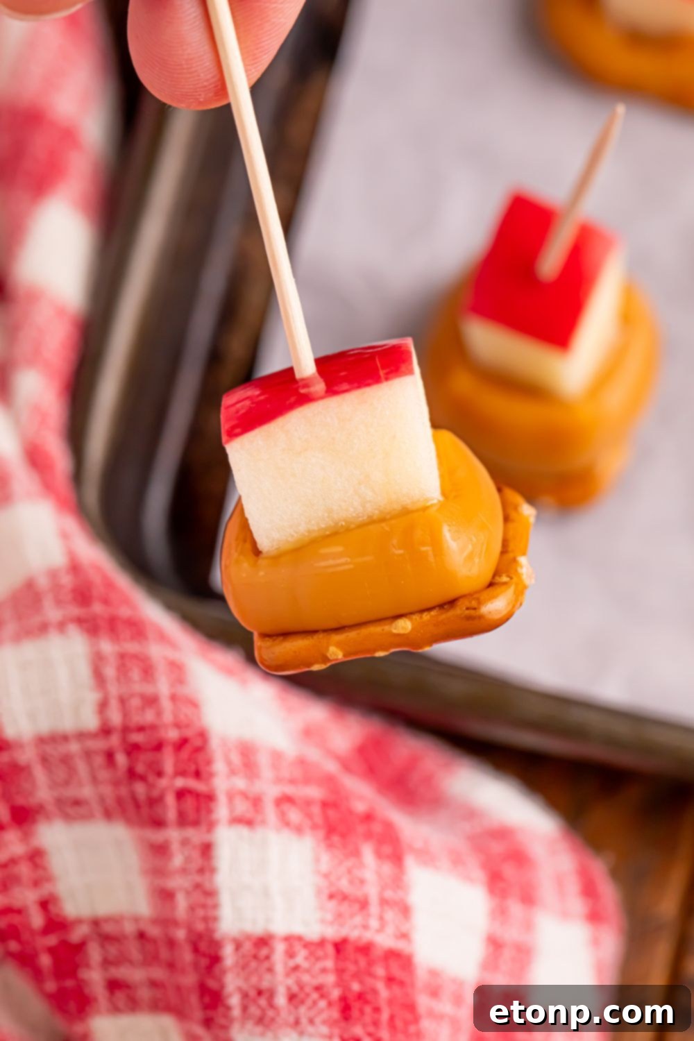 Sweet and Salty Caramel Apple Pretzel Bites 17 Caramel Apple Pretzel Bite being held by toothpick above tray with more