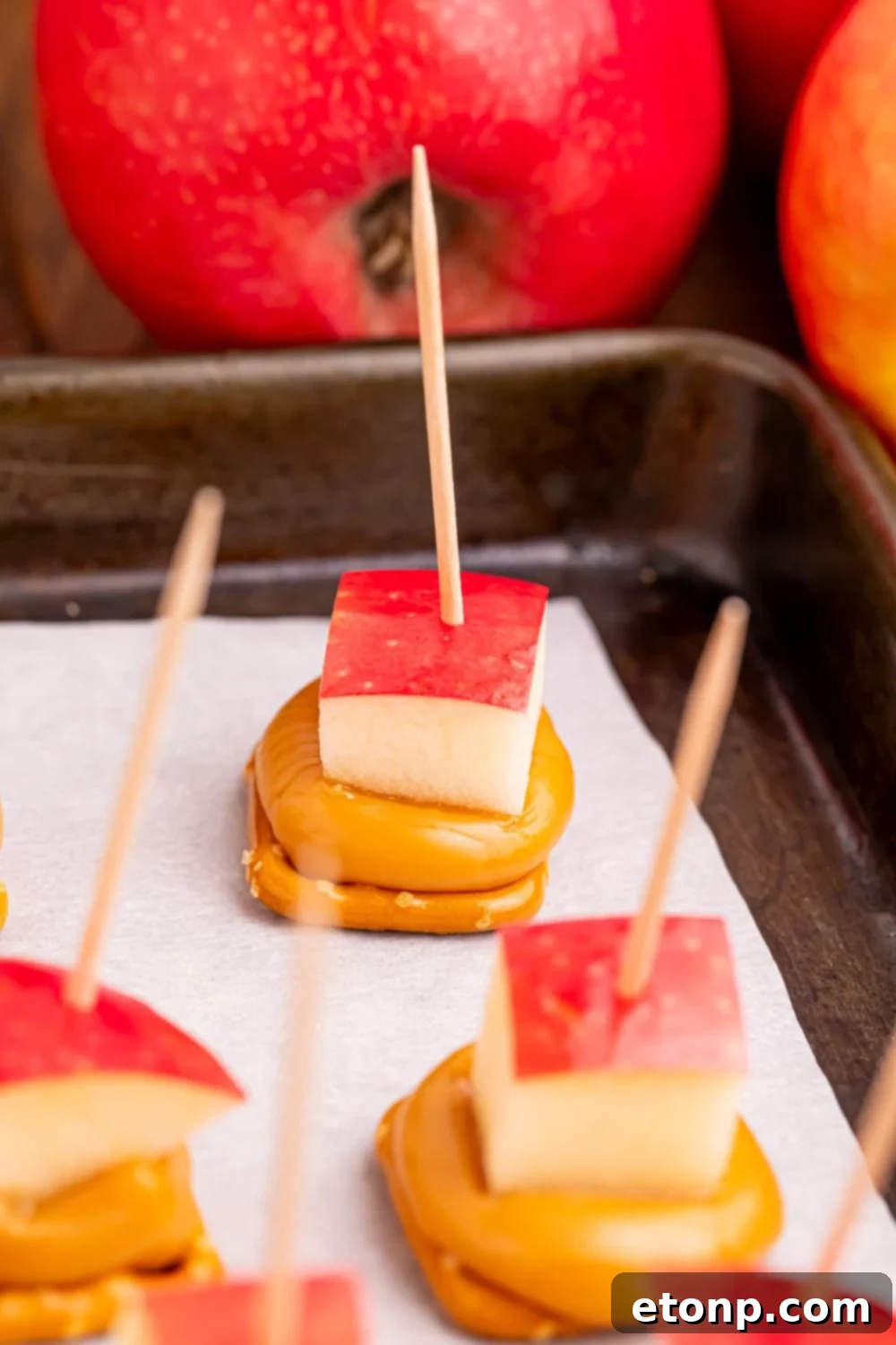Sweet and Salty Caramel Apple Pretzel Bites 18 caramel apple treats with toothpicks poking in sitting on a baking tray on table