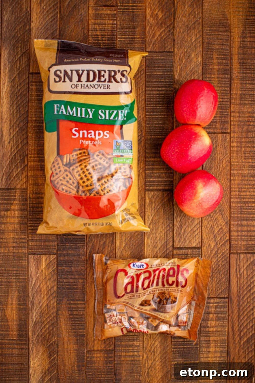 Sweet and Salty Caramel Apple Pretzel Bites 5 Caramel Apple Pretzel Bite ingredients on wooden table: bag of pretzels, apple, caramels in bag