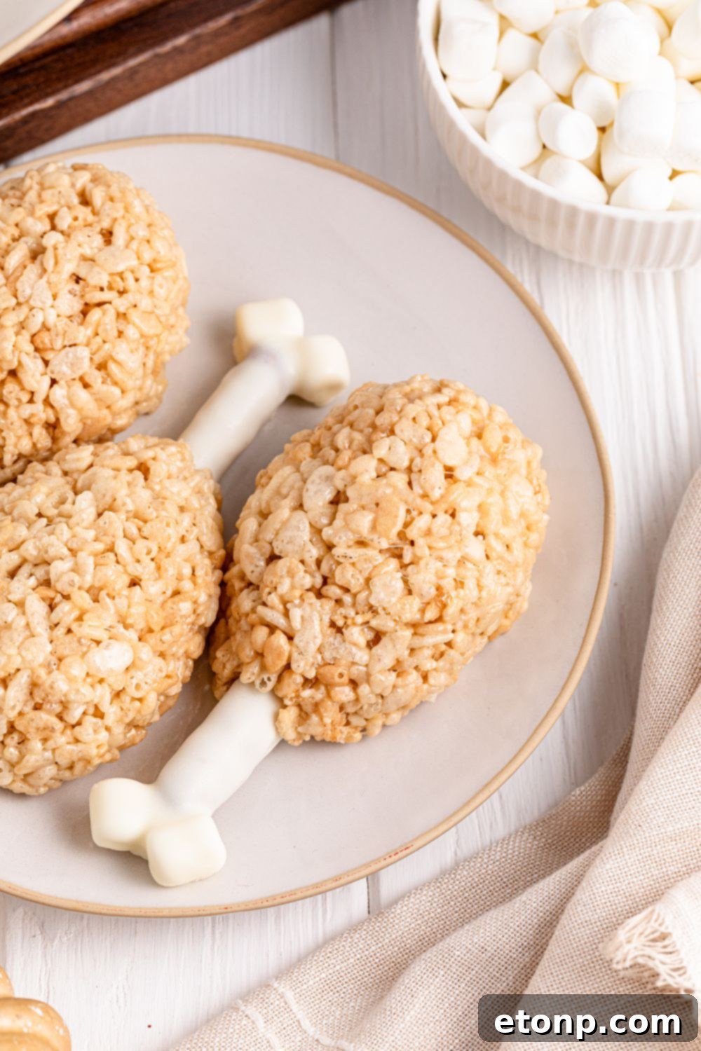 Rice Krispie Treat Turkey Legs on a white plate with bowl of mini marshmallows to the side 