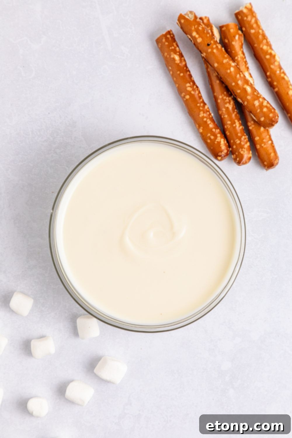 melted white chocolate in a bowl on table with broken pretzel rods on the side 