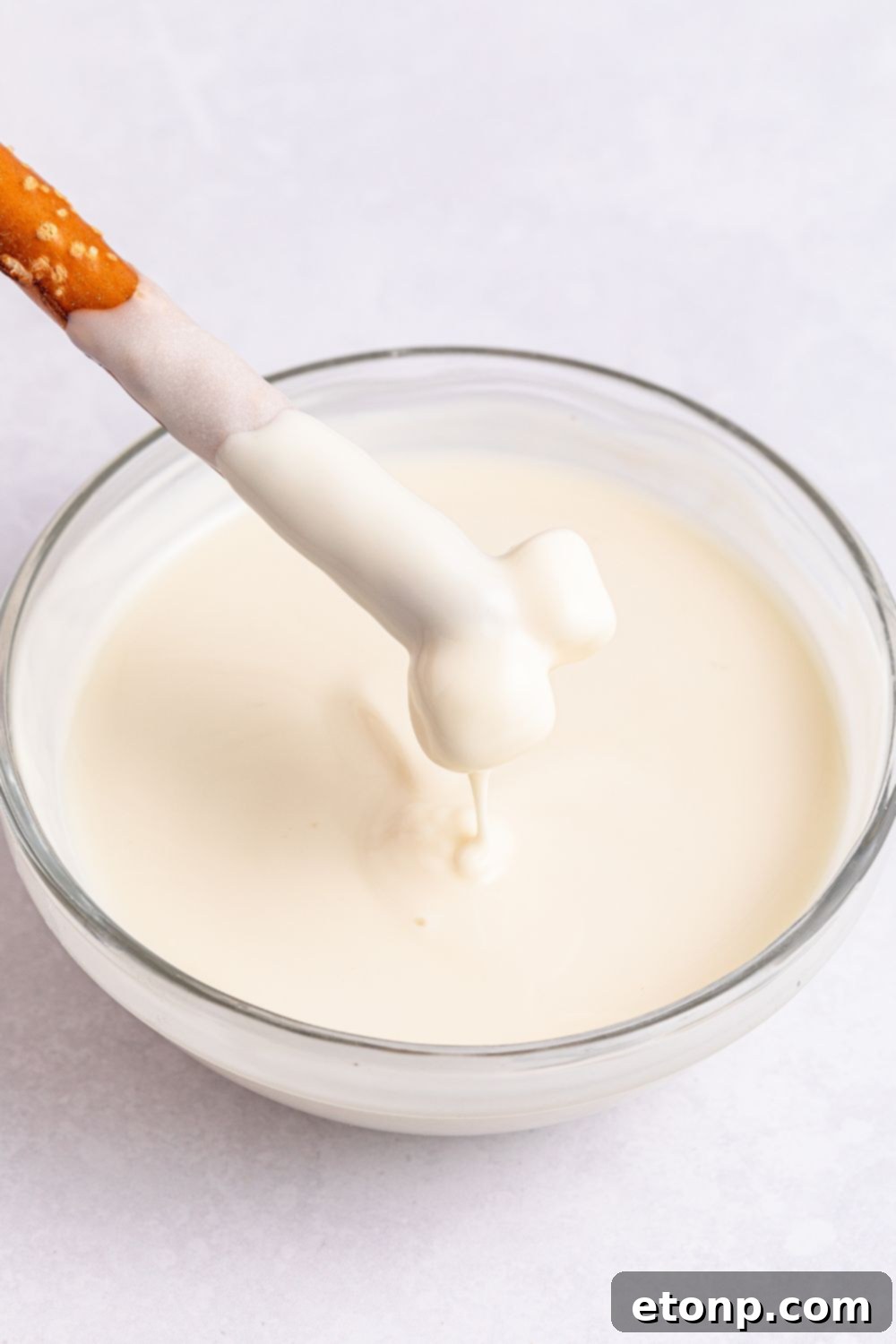 melted white chocolate with a pretzel being dipped in it 