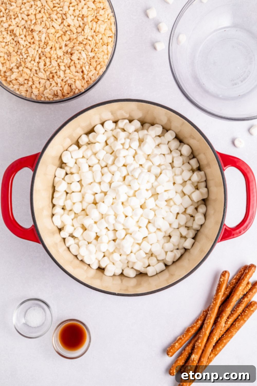 mini marshmallows in a large pot on table with cereal, pretzels and more around it on table