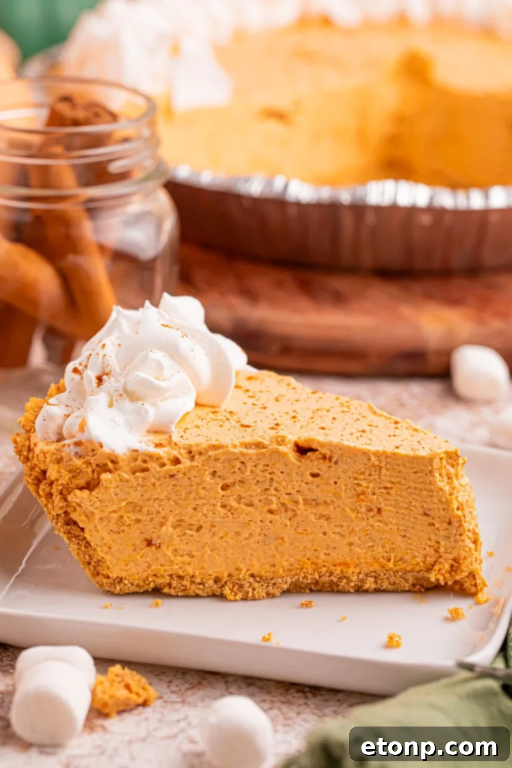 A pristine slice of Marshmallow Pumpkin Pie elegantly presented on a plate, with the remainder of the pie visible in the background on a tastefully decorated table, poised gracefully for serving.