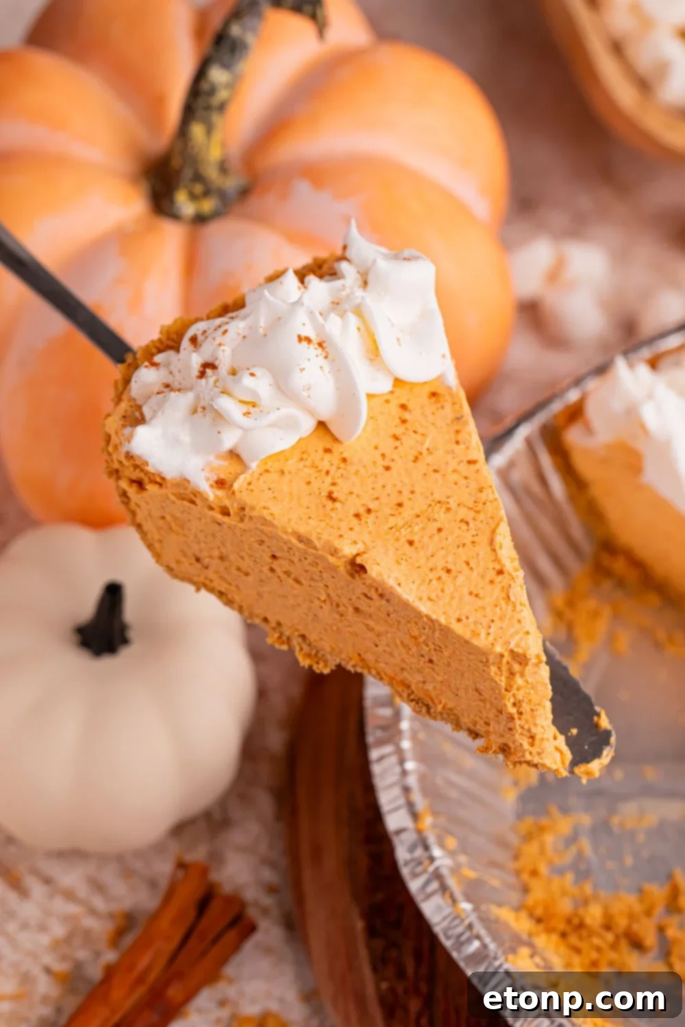 A spatula delicately lifting a perfect slice of Marshmallow Pumpkin Pie from its pie plate, with the harmonious remainder of the pie still intact, elegantly poised for further serving.