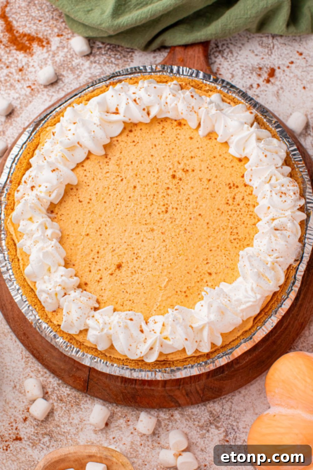 A fully prepared Marshmallow Pumpkin Pie elegantly placed on a table, beautifully adorned with a generous scattering of mini marshmallows and thoughtfully surrounded by charming fall decor, creating a truly festive and inviting display.