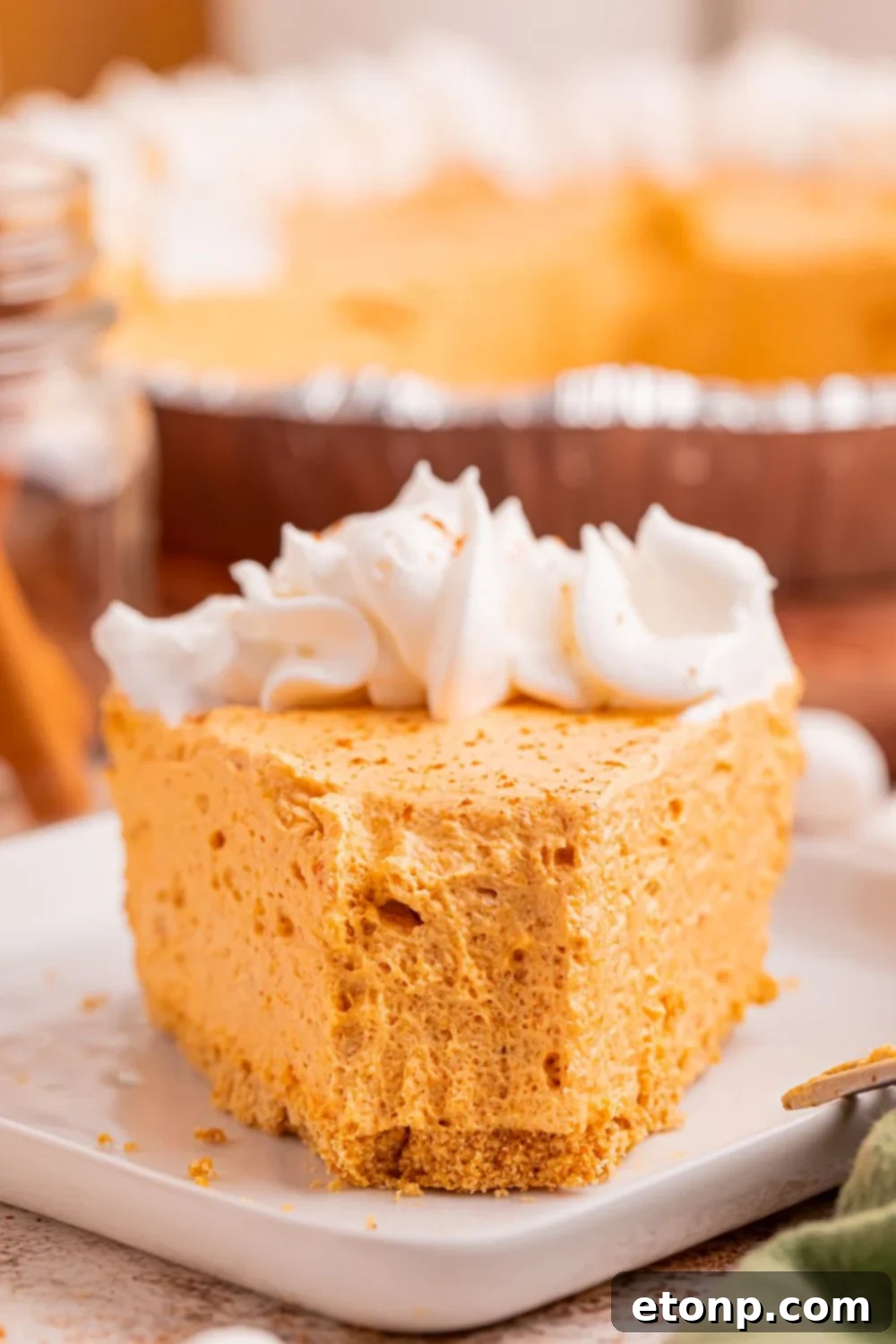A charming front view of a delectable slice of Marshmallow Pumpkin Pie presented beautifully on a table, with a fork already taking a delicious bite, irresistibly emphasizing its inviting and airy texture.