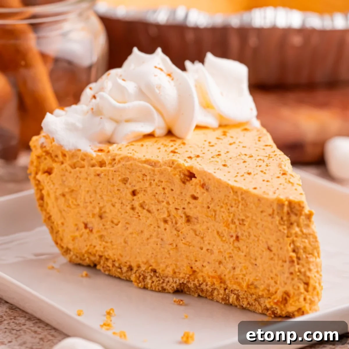 A single slice of Marshmallow Pumpkin Pie artfully placed on a white plate, surrounded by a delicate scattering of graham cracker crumbs, hinting at its delicious, buttery crust.