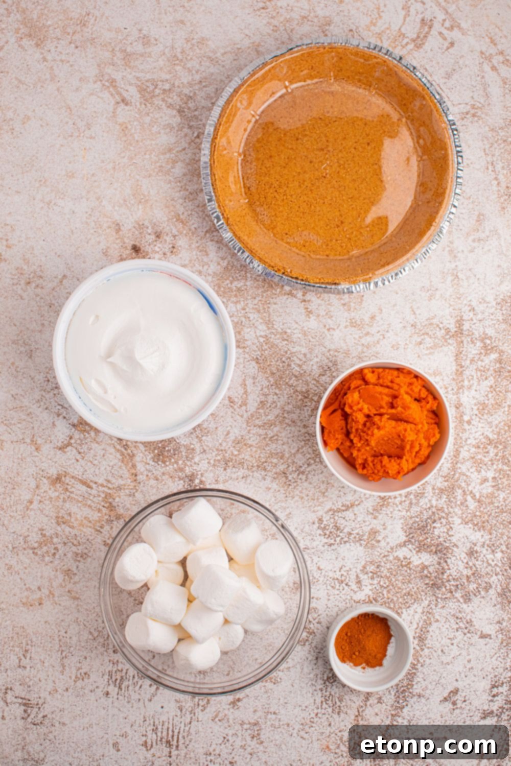 A charming tableau of ingredients for Marshmallow Pumpkin Pie, meticulously arranged in individual serving bowls on a wooden table, featuring vibrant marshmallows, rich pumpkin puree, and aromatic spices, all ready for the preparation process.