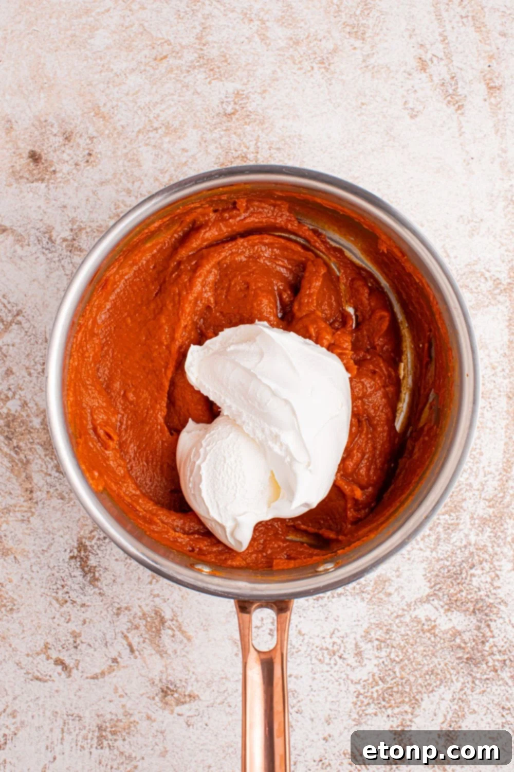 The warm marshmallow and pumpkin mixture cooling gracefully in a saucepan, with a pristine dollop of Cool Whip delicately perched on top of the pumpkin mixture, awaiting to be gently folded in to create a light and fluffy pie filling.