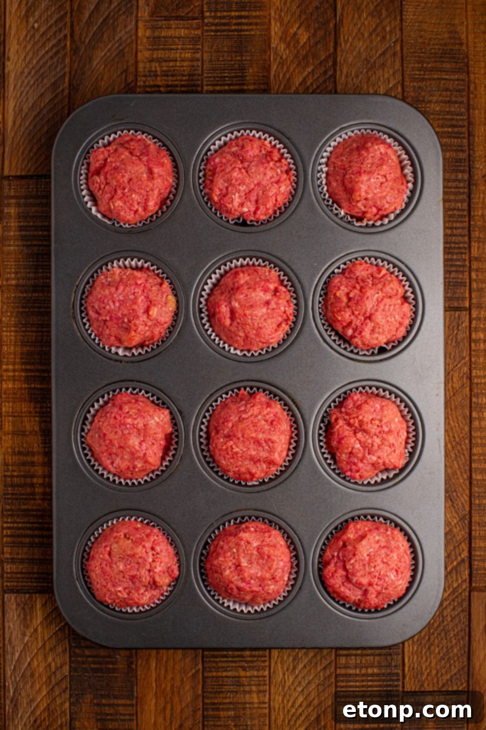 raw meatloaf in a muffin tin tray sitting on table