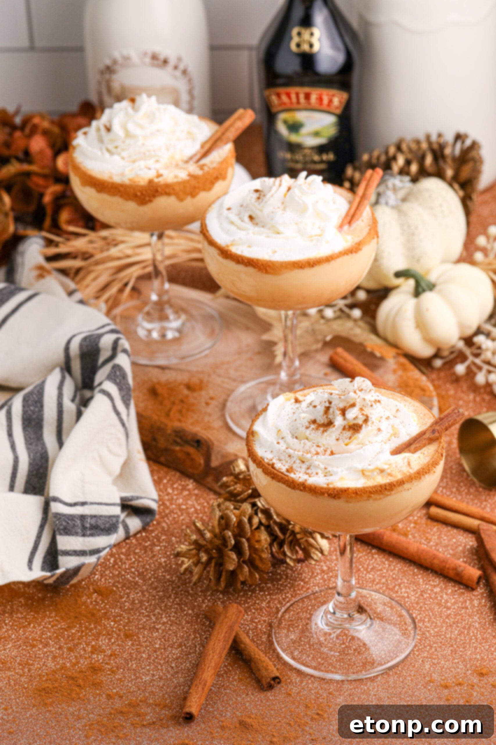 glasses of pumpkin martinis on table with bottles of alcohol to show ingredients in it in the background and fall decor on table