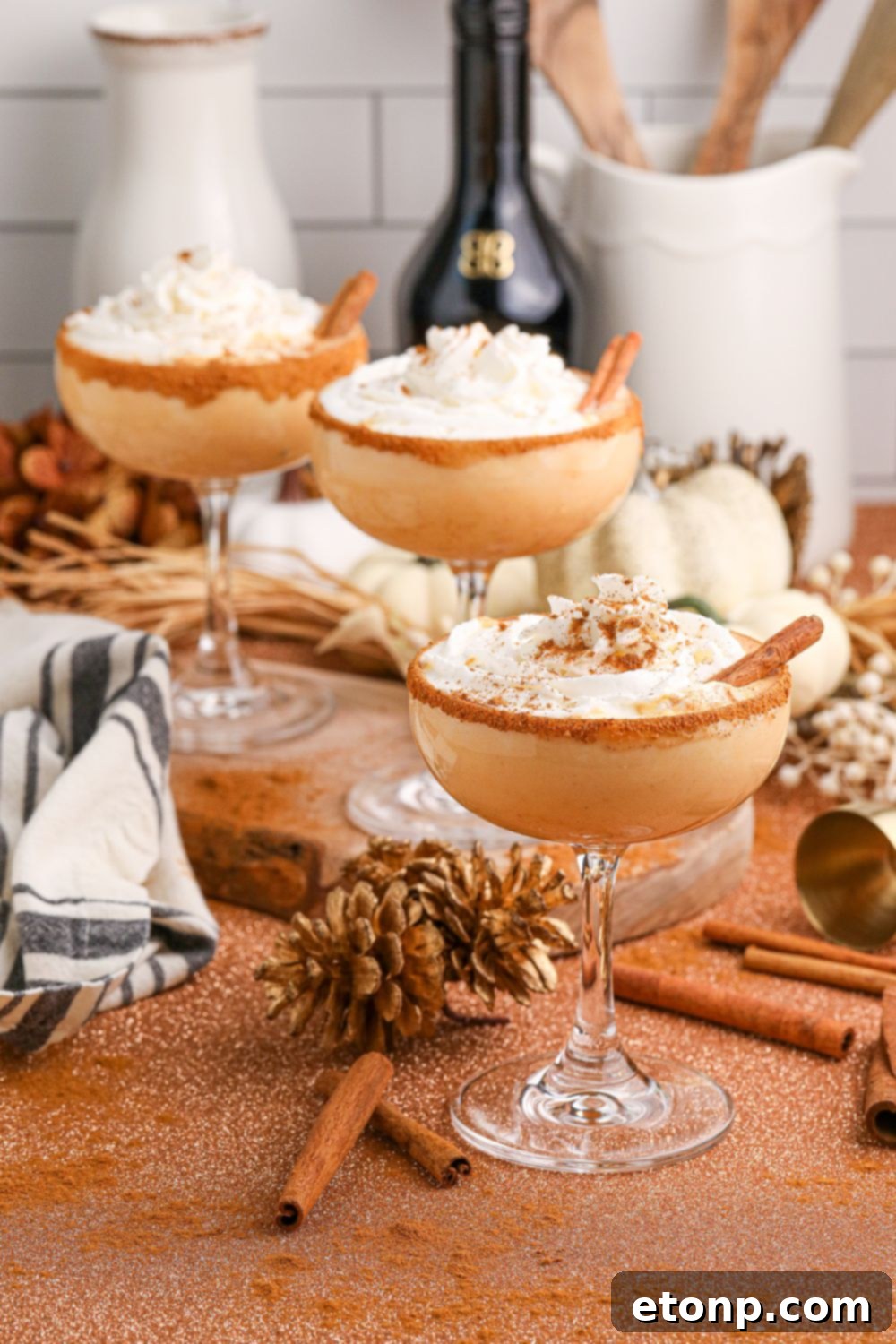 glasses of pumpkin martinis on table with bottles of alcohol to show ingredients in it in the background and fall decor on table