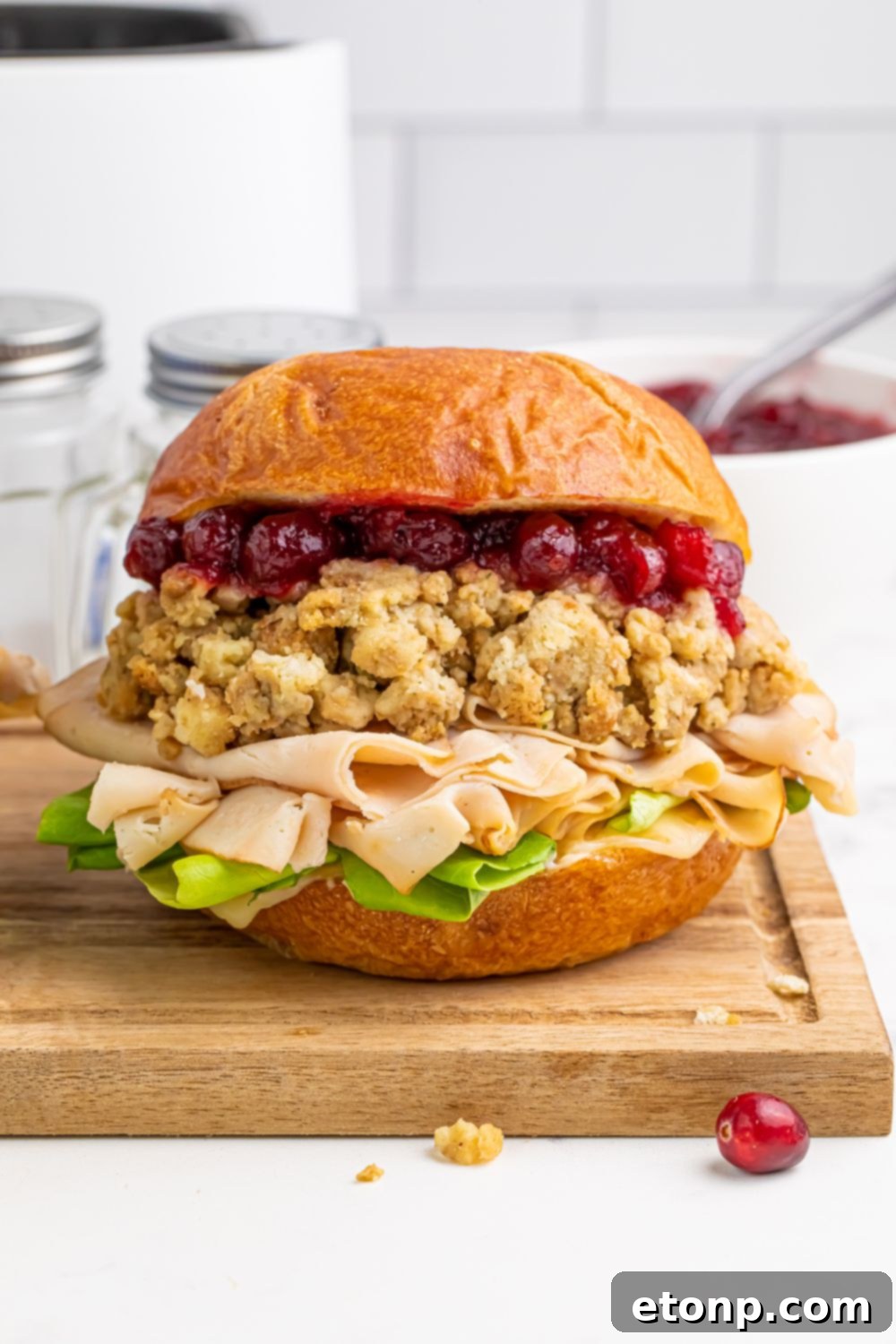 wooden cutting board on table with a turkey sandwich sitting on it with some crumbs and cranberries scattered on table