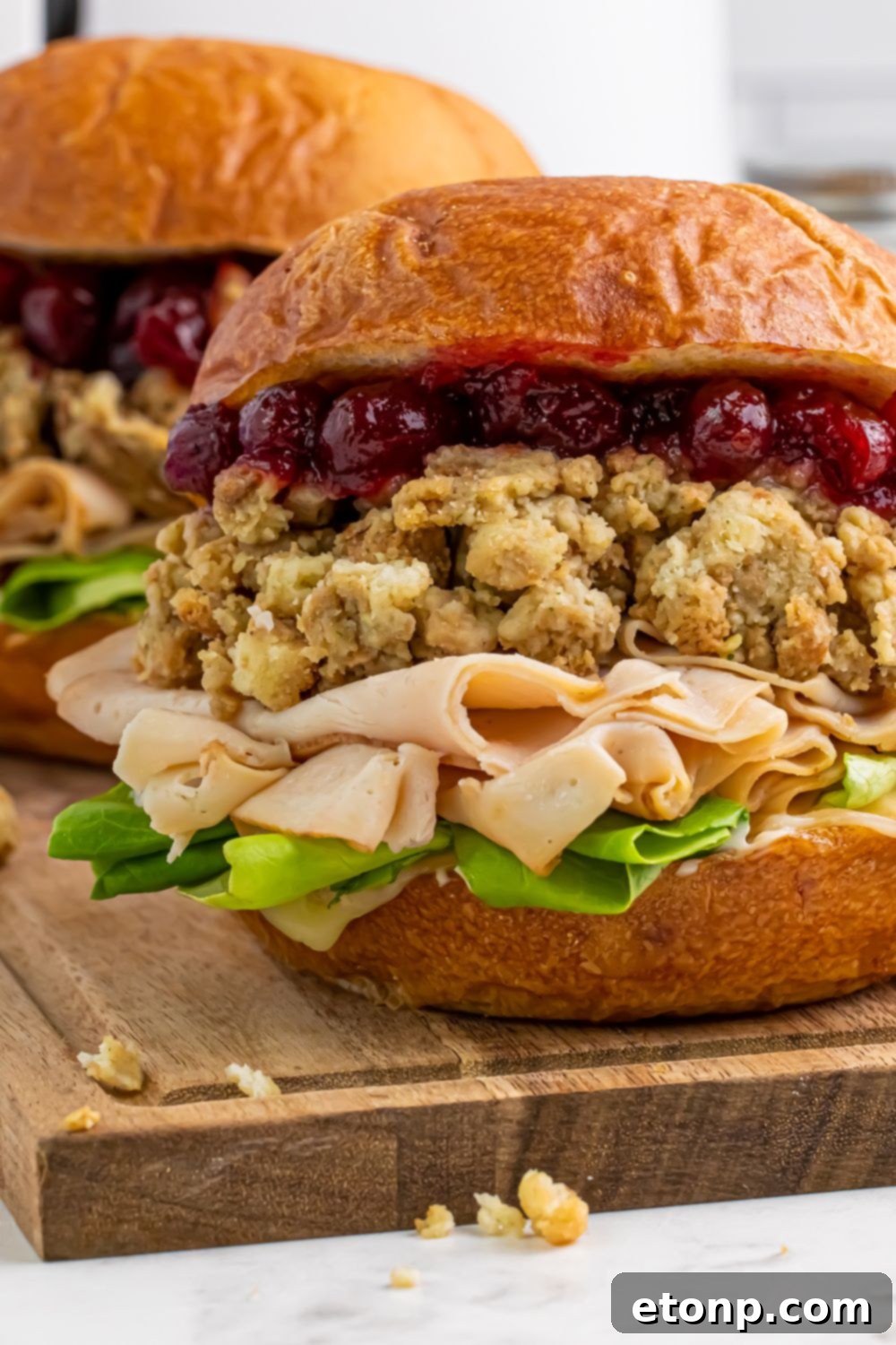 Leftover Turkey Sandwich on table with a close up of the meat, lettuce, stuffing and cranberry sauce on the bun 