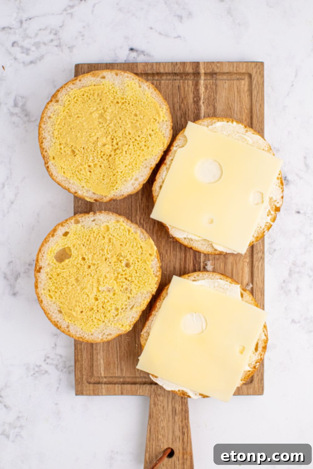 brioche buns sliced in half topped with mayo, mustard and Swiss cheese