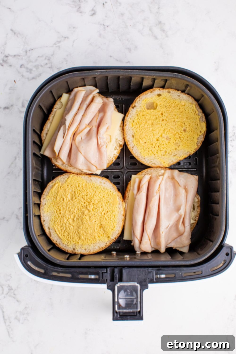 air fryer with turkey sandwiches open faced inside the basket 