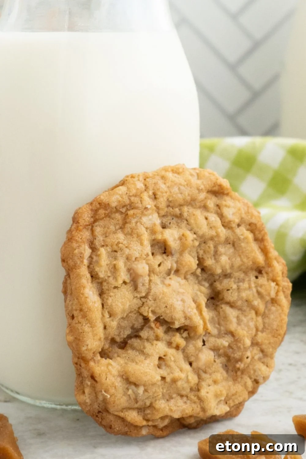 Chewy Toffee Oatmeal Cookies 12 A single Oatmeal Toffee Cookie delicately balanced on the rim of a glass of milk on a table, creating a classic and inviting scene.