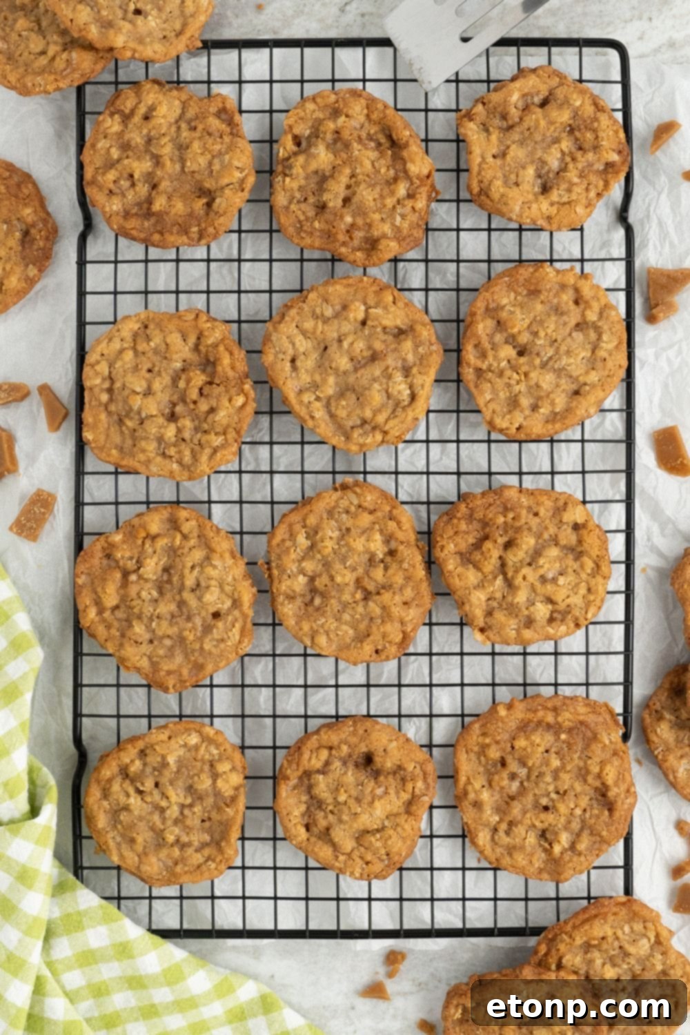 Chewy Toffee Oatmeal Cookies 14 Freshly baked Oatmeal Toffee Cookies cooling on a wire rack on a table, with a neatly folded green towel beside them.