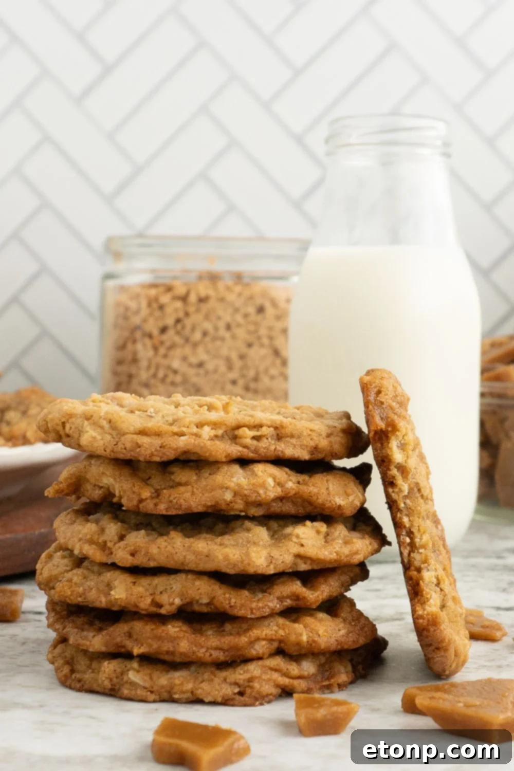 Chewy Toffee Oatmeal Cookies 15 A charming stack of Oatmeal Toffee Cookies, with a tall glass of milk positioned invitingly behind them on a table, ready for a delightful snack.