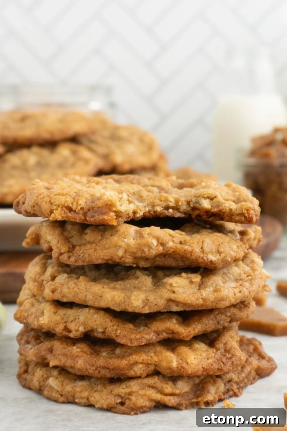Chewy Toffee Oatmeal Cookies 16 A stack of golden toffee chip cookies, with one cookie having a bite taken out of it, showcasing its delicious texture and generous amount of toffee.