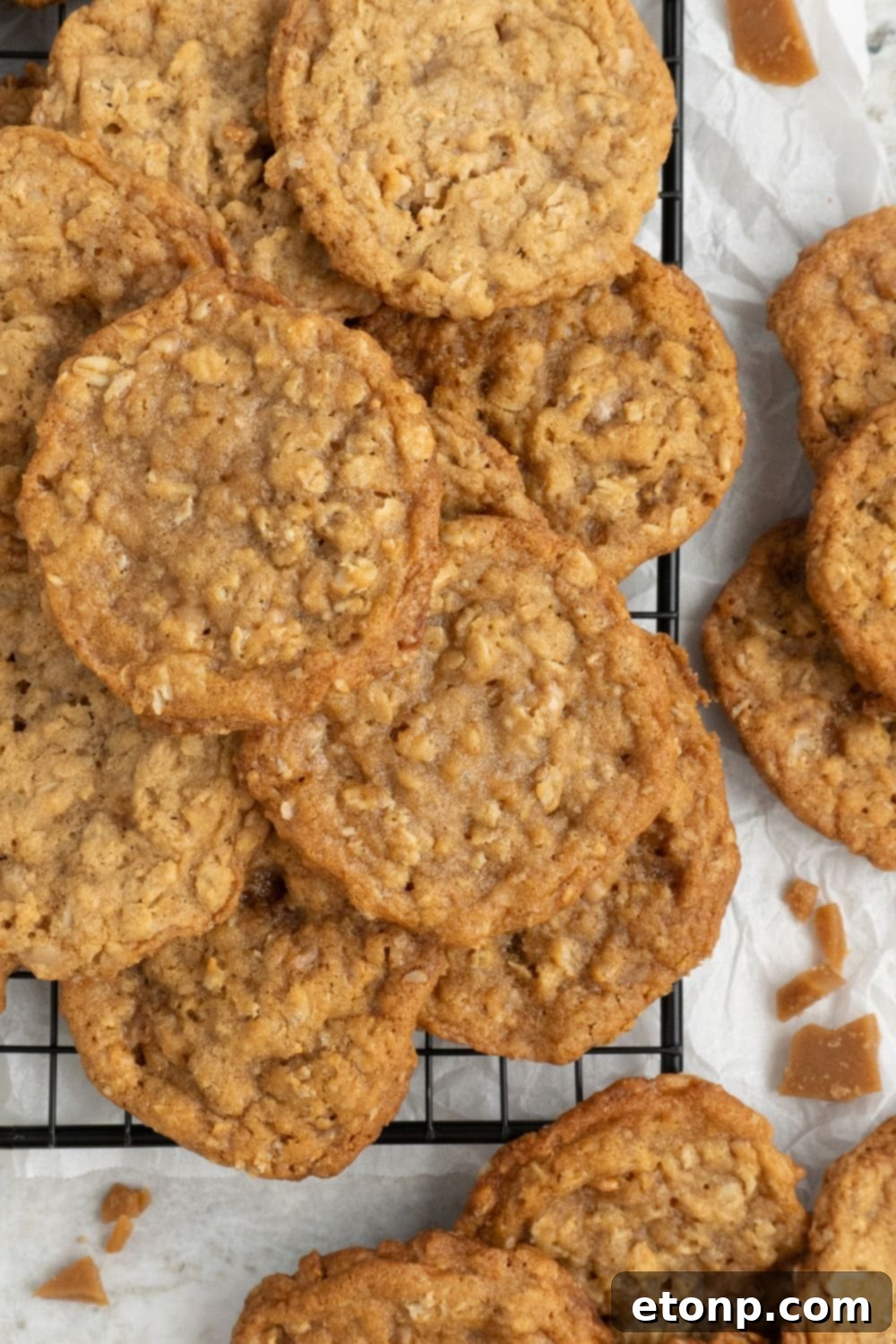 Chewy Toffee Oatmeal Cookies 3 Freshly baked Oatmeal Toffee Cookies cooling on a wire rack, with more cookies casually placed around the tray on a wooden table, emphasizing their abundance.