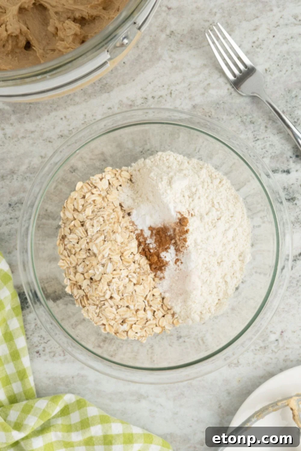 Chewy Toffee Oatmeal Cookies 7 A glass bowl containing all the dry ingredients for Oatmeal Toffee Cookies – oats, flour, and spices – mixed together on a table.