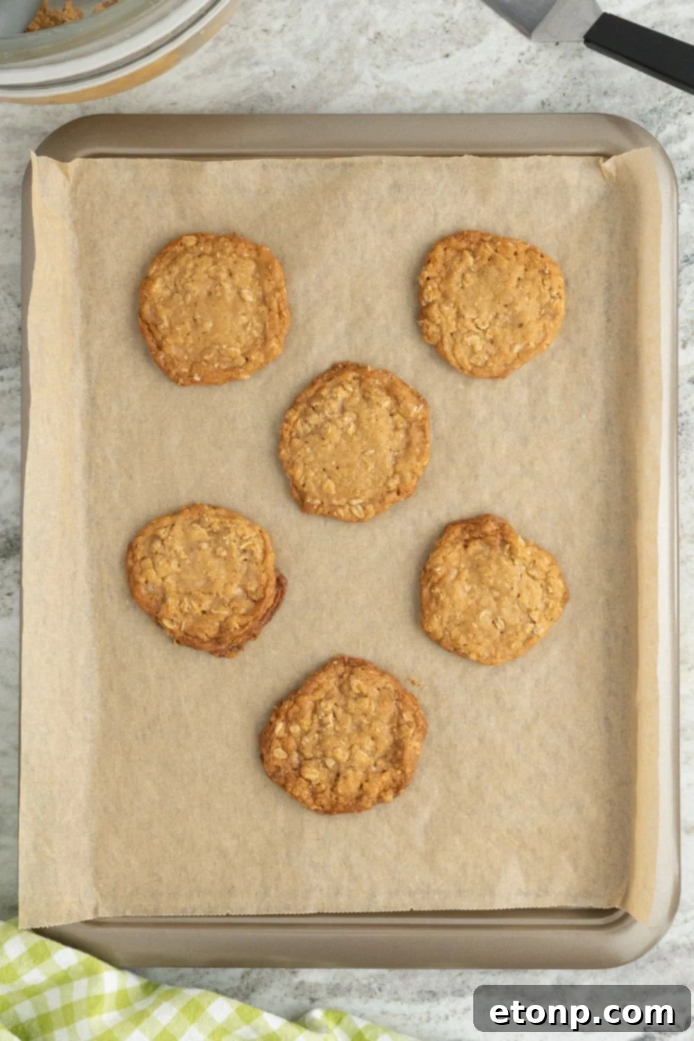 Chewy Toffee Oatmeal Cookies 10 Freshly baked Oatmeal Toffee Cookies on a parchment-lined baking tray, with golden edges and soft centers, just out of the oven.