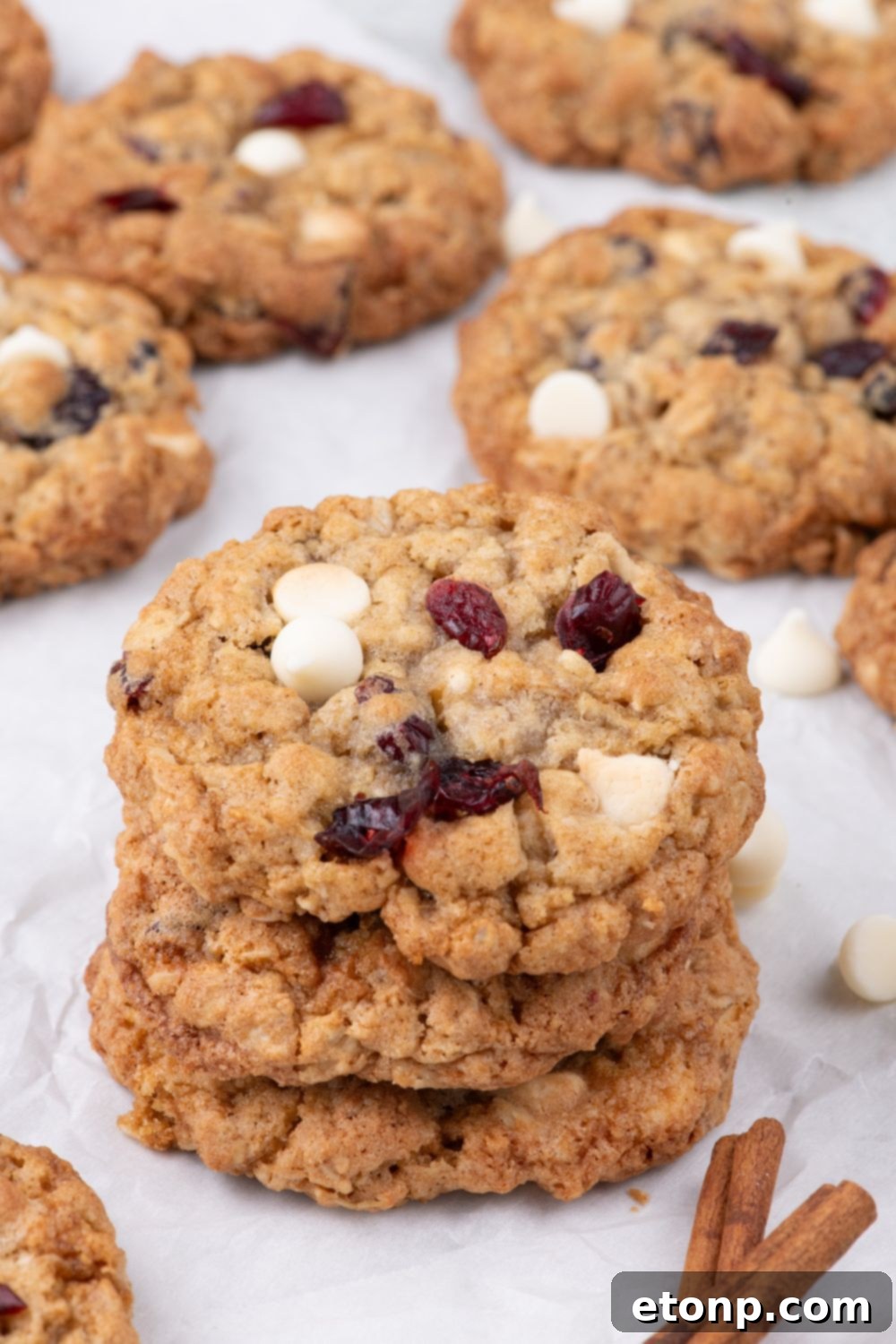 White Chocolate Cranberry Oatmeal Cookies stacked on table with some cookies spread out on counter around the stack 