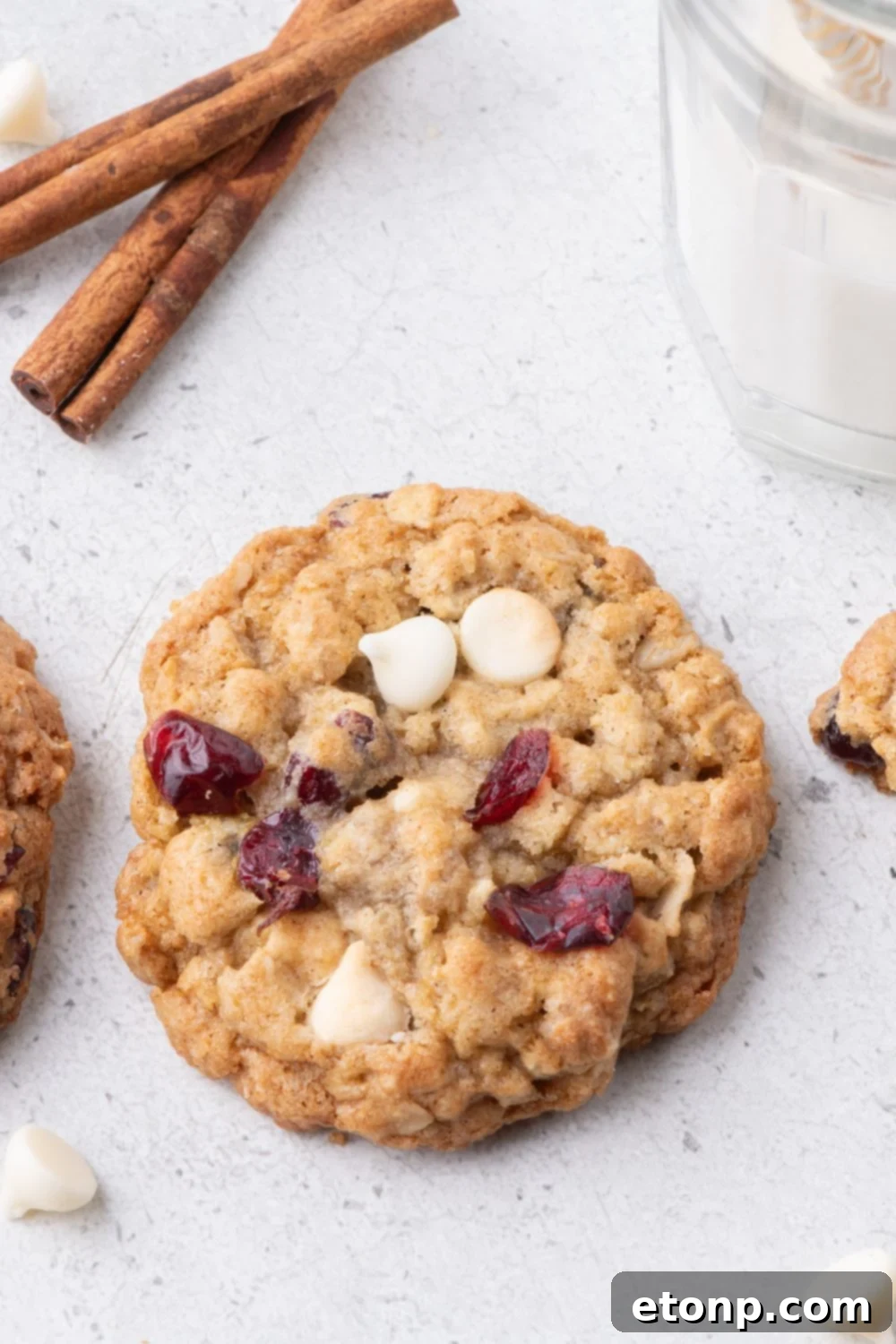 White Chocolate Cranberry Oatmeal Cookies on table with a glass of milk beside the cookie and cinnamon sticks 